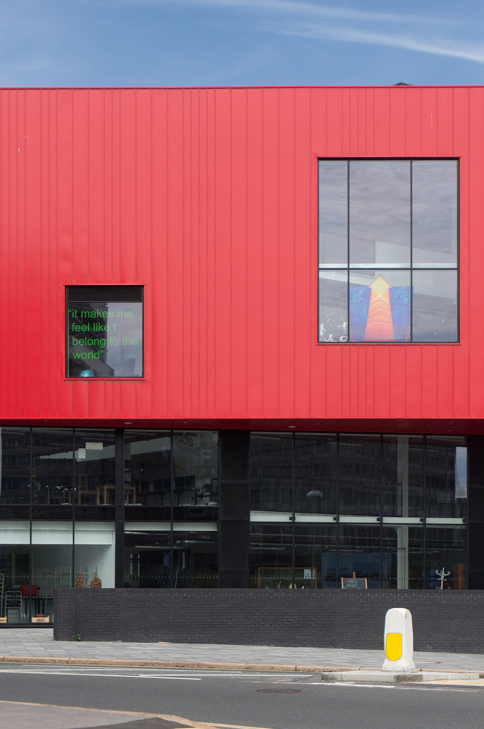 Close up view of the elevation, with industrial red steel cladding sitting above a glass and black brick plinth